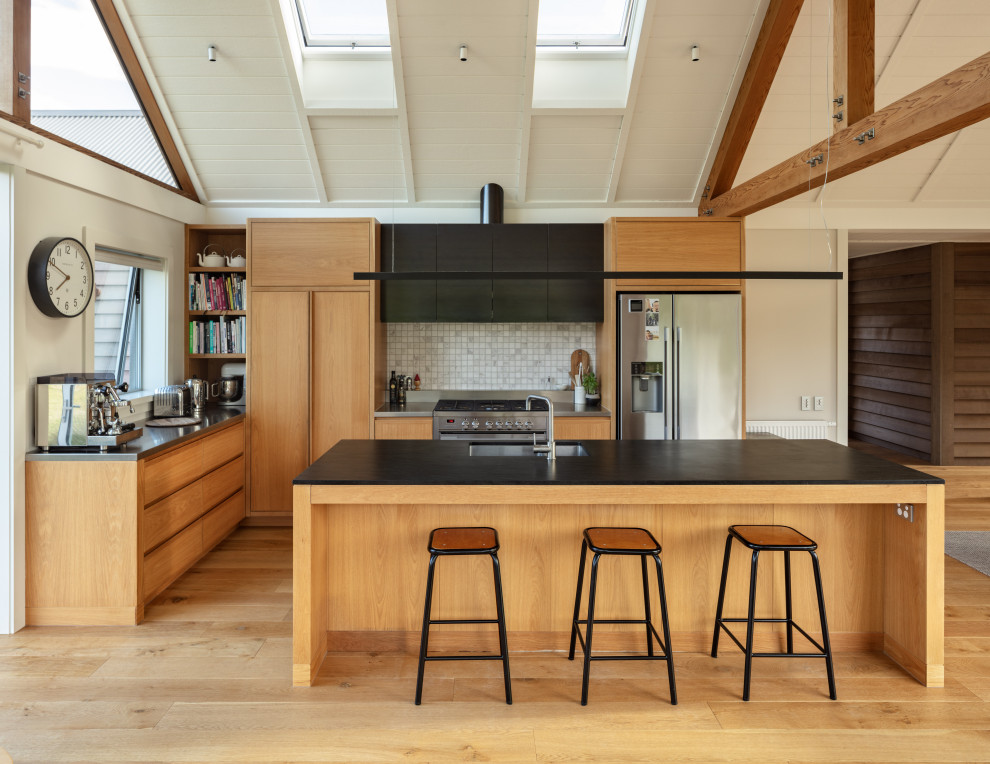 Photo of a contemporary u-shaped open plan kitchen in Dunedin with a submerged sink, flat-panel cabinets, engineered stone countertops, grey splashback, stainless steel appliances, medium hardwood flooring, an island, brown floors, black worktops, exposed beams, a timber clad ceiling and a vaulted ceiling.