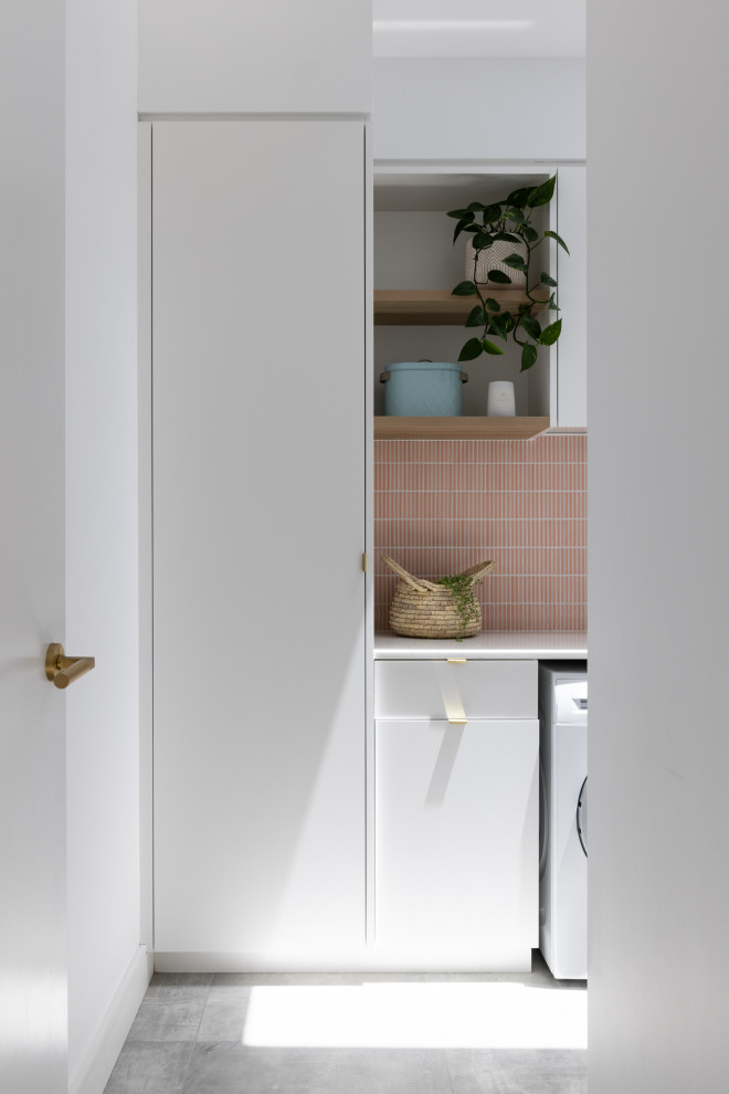 This is an example of a contemporary single-wall laundry room in Sydney with an undermount sink, flat-panel cabinets, white cabinets, quartz benchtops, pink splashback, porcelain splashback, white walls, porcelain floors, a side-by-side washer and dryer, grey floor and white benchtop.