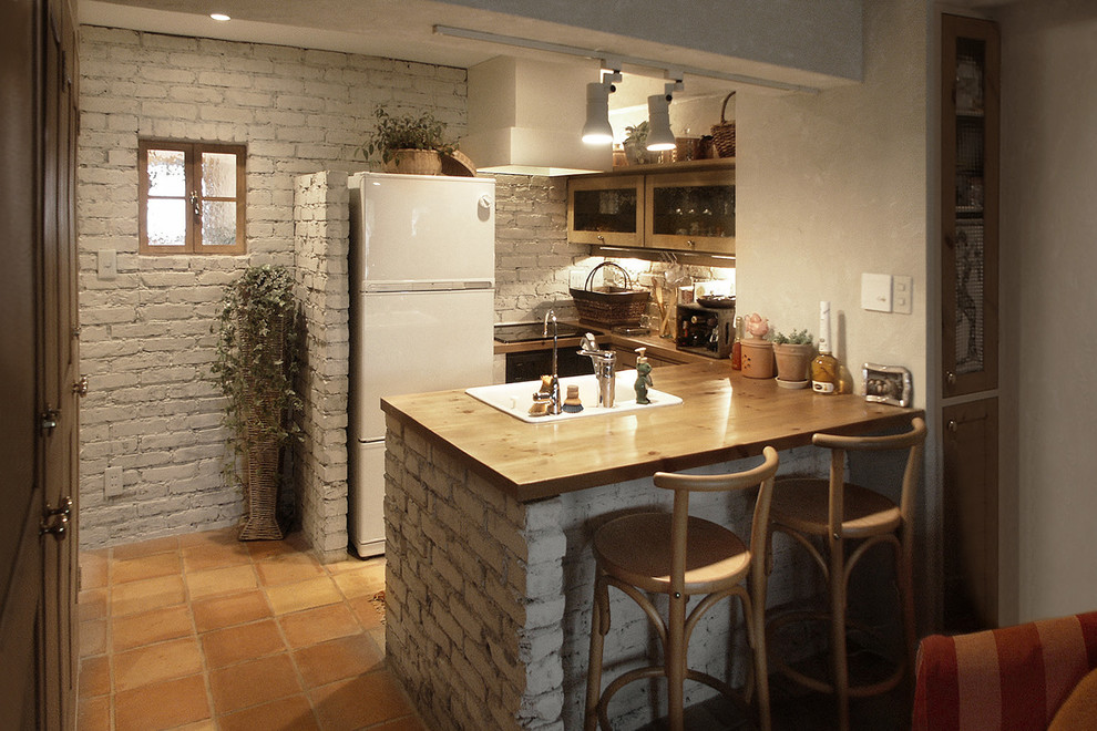 Small country u-shaped kitchen in Tokyo with a single-bowl sink, wood benchtops, terra-cotta floors, a peninsula, orange floor and brown benchtop.