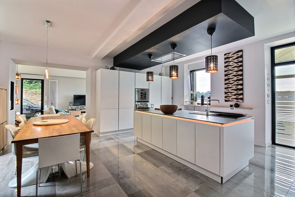 Inspiration for a contemporary galley eat-in kitchen in Brest with a drop-in sink, flat-panel cabinets, white cabinets, white splashback, black appliances, with island, grey floor and black benchtop.