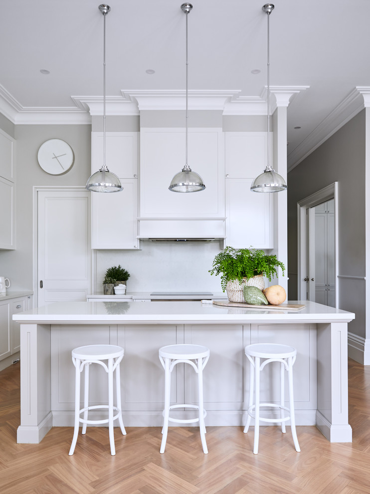 Design ideas for a mid-sized traditional l-shaped kitchen in Melbourne with shaker cabinets, white cabinets, quartz benchtops, white splashback, stone slab splashback, with island, white benchtop, medium hardwood floors and brown floor.