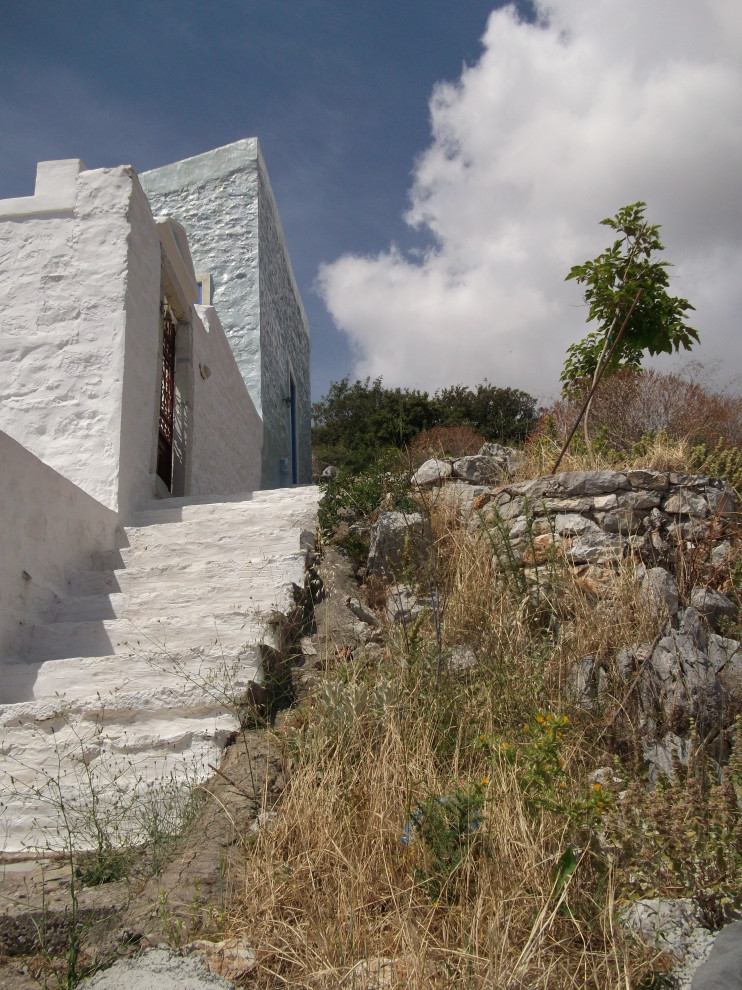 Idée de décoration pour une petite façade de maison bleue méditerranéenne en pierre à un étage avec un toit papillon, un toit en tuile et un toit rouge.