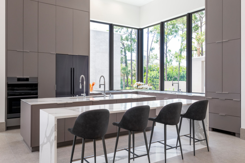 Photo of a mid-sized contemporary l-shaped eat-in kitchen in Other with a drop-in sink, flat-panel cabinets, quartz benchtops, stainless steel appliances, porcelain floors, multiple islands, beige floor, white benchtop and grey cabinets.