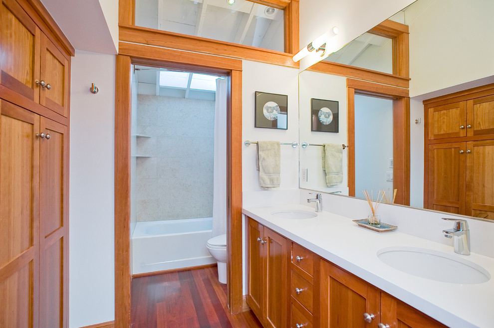 Photo of a small contemporary bathroom in San Francisco with an undermount sink, shaker cabinets, medium wood cabinets, engineered quartz benchtops, an alcove tub, a one-piece toilet, beige tile, porcelain tile, white walls, medium hardwood floors and white benchtops.
