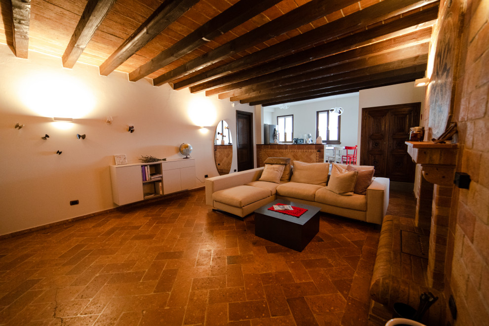 This is an example of a large country formal loft-style living room in Milan with white walls, terra-cotta floors, a standard fireplace, a wall-mounted tv, orange floor, timber and brick walls.