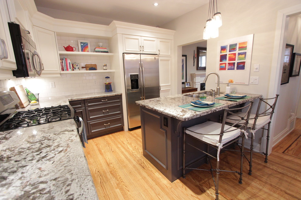 This is an example of a mid-sized eclectic l-shaped separate kitchen in Toronto with an undermount sink, recessed-panel cabinets, white cabinets, granite benchtops, white splashback, subway tile splashback, stainless steel appliances, light hardwood floors and a peninsula.