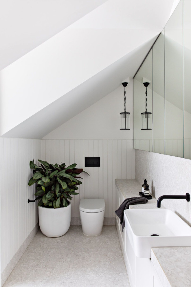 Cette image montre un WC et toilettes design avec des portes de placard blanches, un mur blanc, un sol en terrazzo, un plan de toilette en carrelage, du lambris, des carreaux de porcelaine et un sol gris.