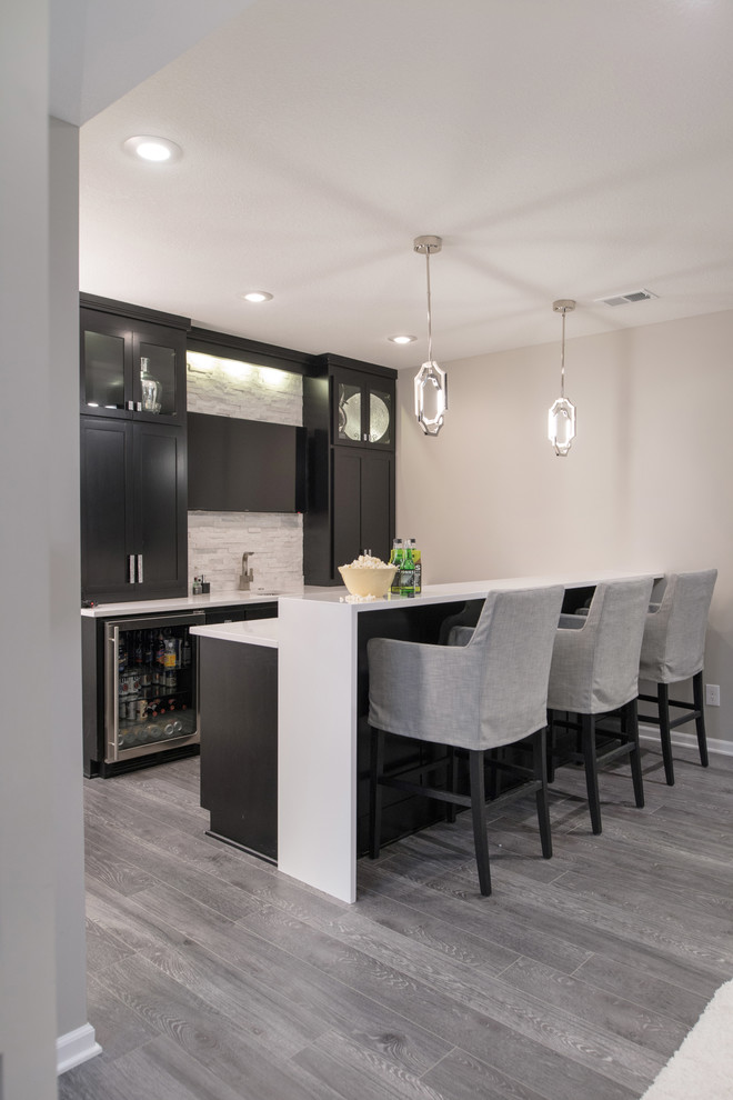Inspiration for a large transitional single-wall seated home bar in Kansas City with an undermount sink, recessed-panel cabinets, black cabinets, quartz benchtops, white splashback, matchstick tile splashback, vinyl floors and grey floor.