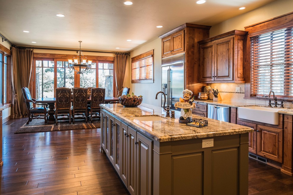 This is an example of a mid-sized country eat-in kitchen in Other with a farmhouse sink, raised-panel cabinets, medium wood cabinets, granite benchtops, stainless steel appliances, dark hardwood floors and with island.