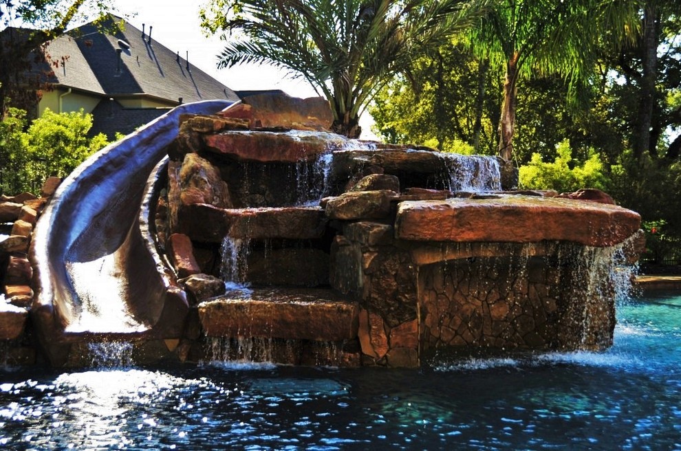 This is an example of a large modern backyard custom-shaped natural pool in Houston with a water feature and stamped concrete.