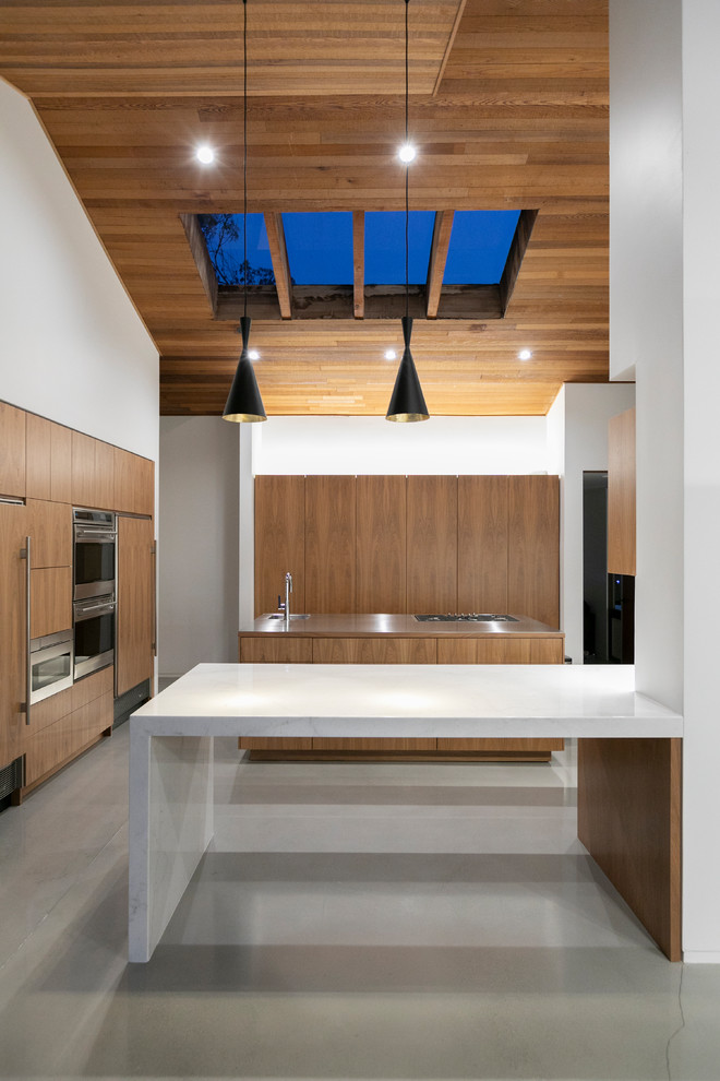 Inspiration for a midcentury kitchen in Los Angeles with a single-bowl sink, flat-panel cabinets, medium wood cabinets, stainless steel appliances, concrete floors, a peninsula, grey floor and white benchtop.