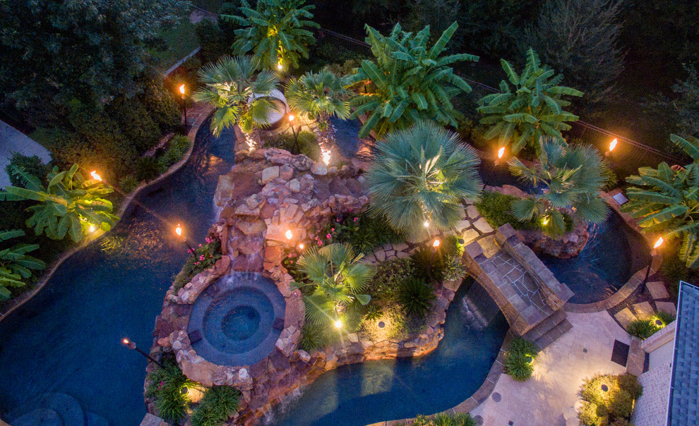 Large tropical backyard custom-shaped pool in Dallas with a water feature and natural stone pavers.