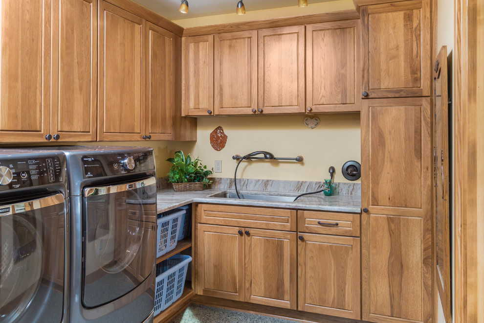 Small arts and crafts l-shaped dedicated laundry room in Other with an undermount sink, raised-panel cabinets, medium wood cabinets, granite benchtops, yellow walls, concrete floors and a side-by-side washer and dryer.