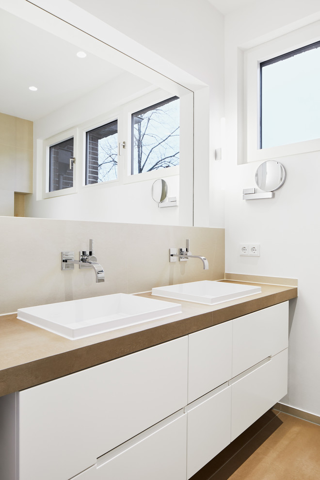 Badezimmer With flächenbündigen Schrankfronten, weißen Schränken, beigen Fliesen, Aufsatzwaschbecken and brauner Waschtischplatte in Cologne