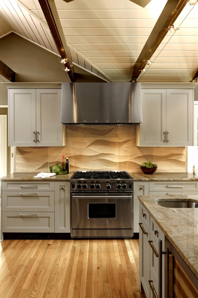Inspiration for a mid-sized transitional l-shaped eat-in kitchen in DC Metro with an undermount sink, recessed-panel cabinets, beige splashback, porcelain splashback, stainless steel appliances, light hardwood floors, a peninsula, beige floor, grey cabinets and granite benchtops.