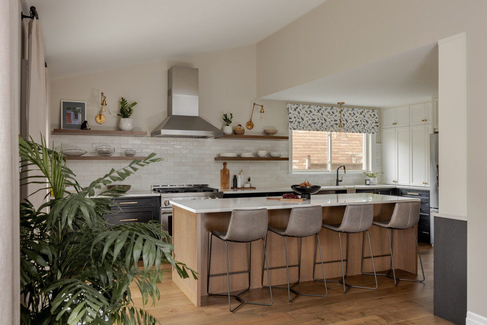 Transitional l-shaped medium tone wood floor, brown floor and vaulted ceiling kitchen photo in Toronto with an undermount sink, shaker cabinets, black cabinets, white backsplash, subway tile backsplash, stainless steel appliances, an island and white countertops