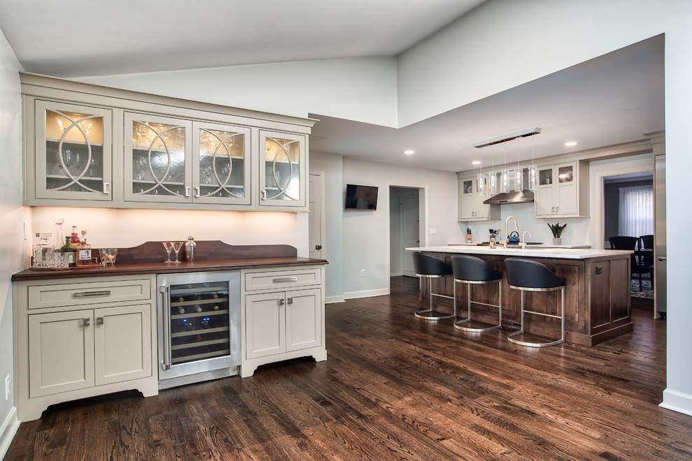 Large transitional l-shaped eat-in kitchen in New York with a farmhouse sink, beaded inset cabinets, beige cabinets, granite benchtops, white splashback, porcelain splashback, stainless steel appliances, painted wood floors, with island, brown floor and white benchtop.