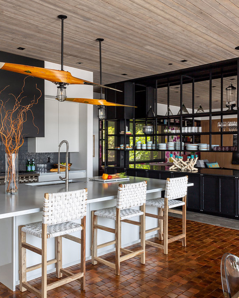 Photo of a large rustic u-shaped kitchen/diner in Los Angeles with a submerged sink, flat-panel cabinets, white cabinets, composite countertops, grey splashback, terracotta splashback, stainless steel appliances, terracotta flooring, an island, orange floors, white worktops and a wood ceiling.