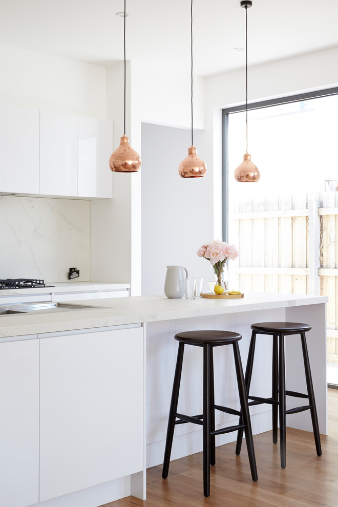 Contemporary galley kitchen in Sydney with white cabinets, marble benchtops, white splashback, stone slab splashback, with island, flat-panel cabinets and medium hardwood floors.