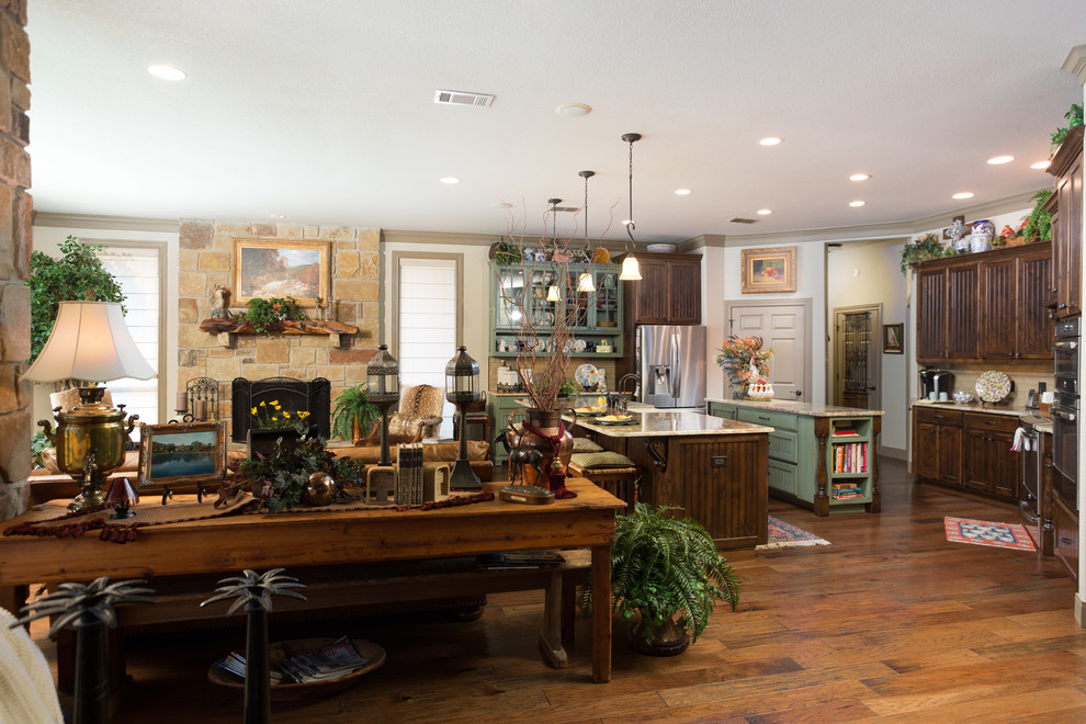 Mid-sized mountain style open concept and u-shaped brown floor and dark wood floor eat-in kitchen photo in Austin with beige walls, a standard fireplace, a stone fireplace, no tv, a farmhouse sink, beaded inset cabinets, medium tone wood cabinets, granite countertops, beige backsplash, ceramic backsplash, stainless steel appliances, two islands and multicolored countertops