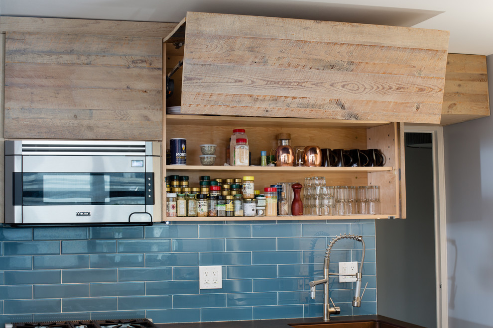 This is an example of a small country u-shaped eat-in kitchen in New York with a farmhouse sink, flat-panel cabinets, distressed cabinets, quartz benchtops, blue splashback, glass tile splashback, stainless steel appliances, ceramic floors and no island.