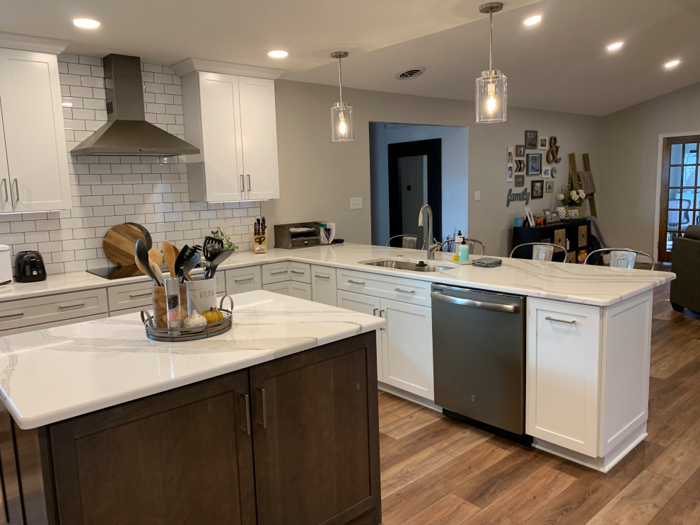 Open concept kitchen - large transitional u-shaped vinyl floor and brown floor open concept kitchen idea with an undermount sink, shaker cabinets, white cabinets, quartz countertops, white backsplash, ceramic backsplash, stainless steel appliances, an island and white countertops