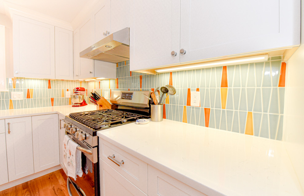 Bild på ett mellanstort 60 tals vit vitt l-kök, med en undermonterad diskho, skåp i shakerstil, vita skåp, bänkskiva i kvarts, blått stänkskydd, stänkskydd i keramik, rostfria vitvaror, mellanmörkt trägolv och en halv köksö