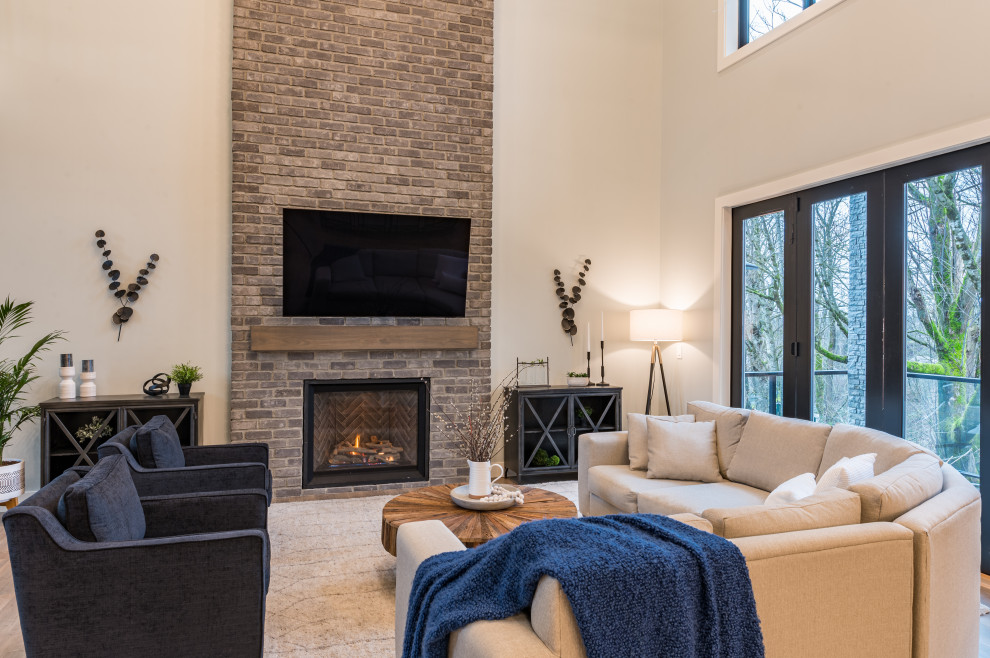 This is an example of a large rural grey and brown open plan living room in Vancouver with white walls, laminate floors, a standard fireplace, a brick fireplace surround, a wall mounted tv, brown floors and brick walls.