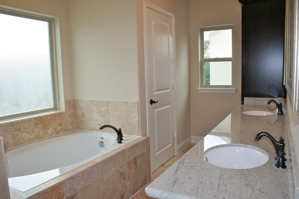 Mid-sized traditional master bathroom in Houston with recessed-panel cabinets, dark wood cabinets, granite benchtops, beige tile, stone tile, a hot tub, an alcove shower, a one-piece toilet, an undermount sink, beige walls and travertine floors.