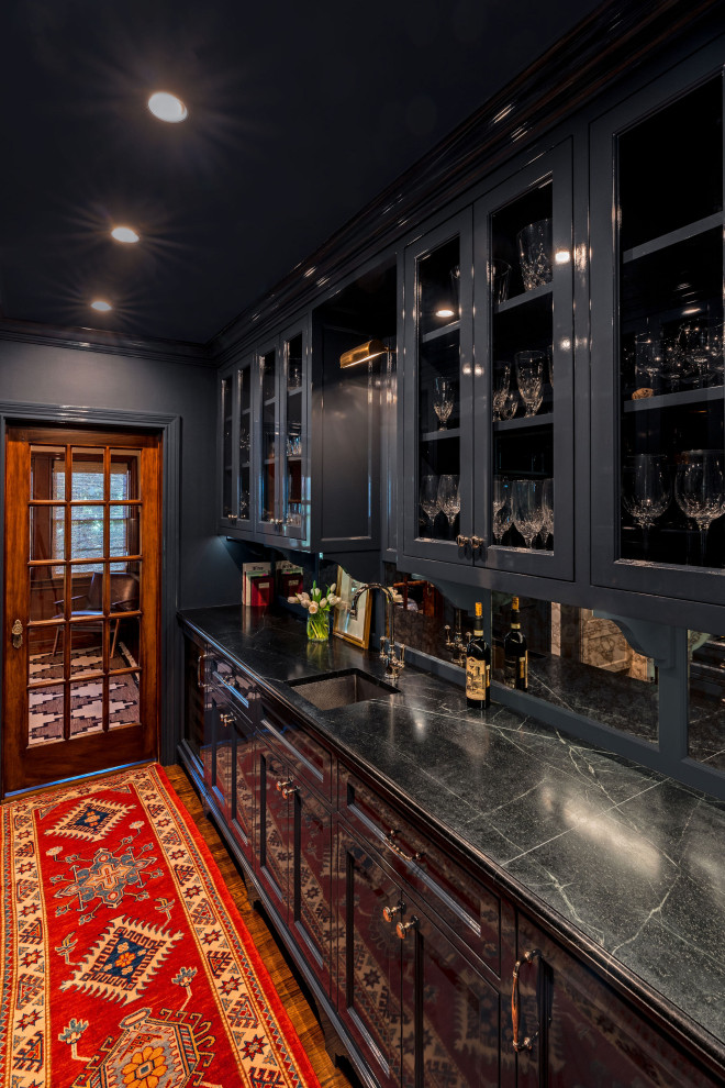 Inspiration for a mid-sized traditional galley wet bar in Houston with an undermount sink, beaded inset cabinets, blue cabinets, soapstone benchtops, mirror splashback, dark hardwood floors, brown floor and black benchtop.
