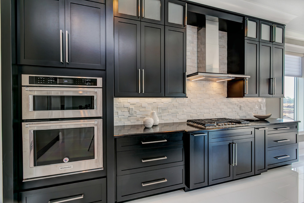 Large trendy l-shaped white floor open concept kitchen photo in Seattle with an undermount sink, shaker cabinets, black cabinets, granite countertops, white backsplash, stone tile backsplash, stainless steel appliances and an island
