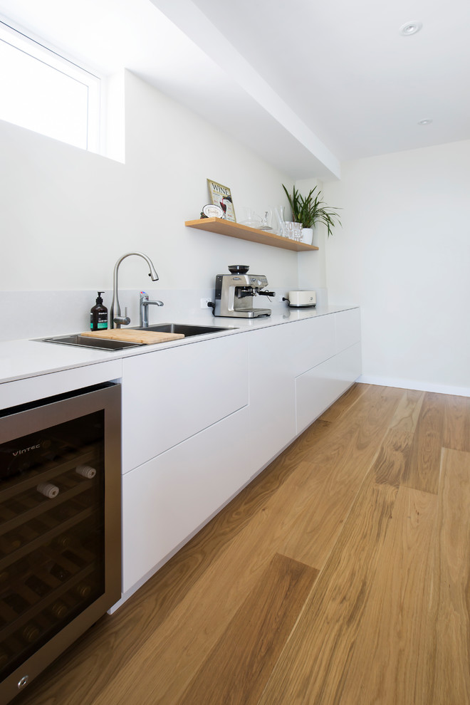 Design ideas for an expansive scandinavian kitchen pantry in Sydney with a double-bowl sink, quartz benchtops, mirror splashback, black appliances and light hardwood floors.
