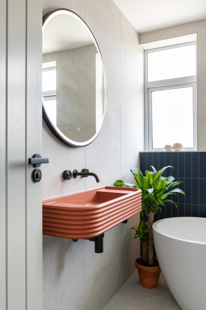 Photo of a mid-sized contemporary kids bathroom in London with a freestanding tub, an open shower, a one-piece toilet, gray tile, porcelain tile, grey walls, porcelain floors, a wall-mount sink, concrete benchtops, grey floor, a hinged shower door, orange benchtops and a single vanity.