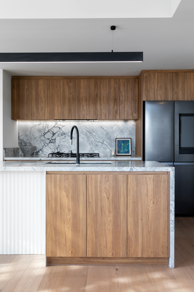 Mid-sized contemporary galley open plan kitchen in Melbourne with an undermount sink, flat-panel cabinets, medium wood cabinets, marble benchtops, grey splashback, marble splashback, black appliances, medium hardwood floors, with island, brown floor and grey benchtop.