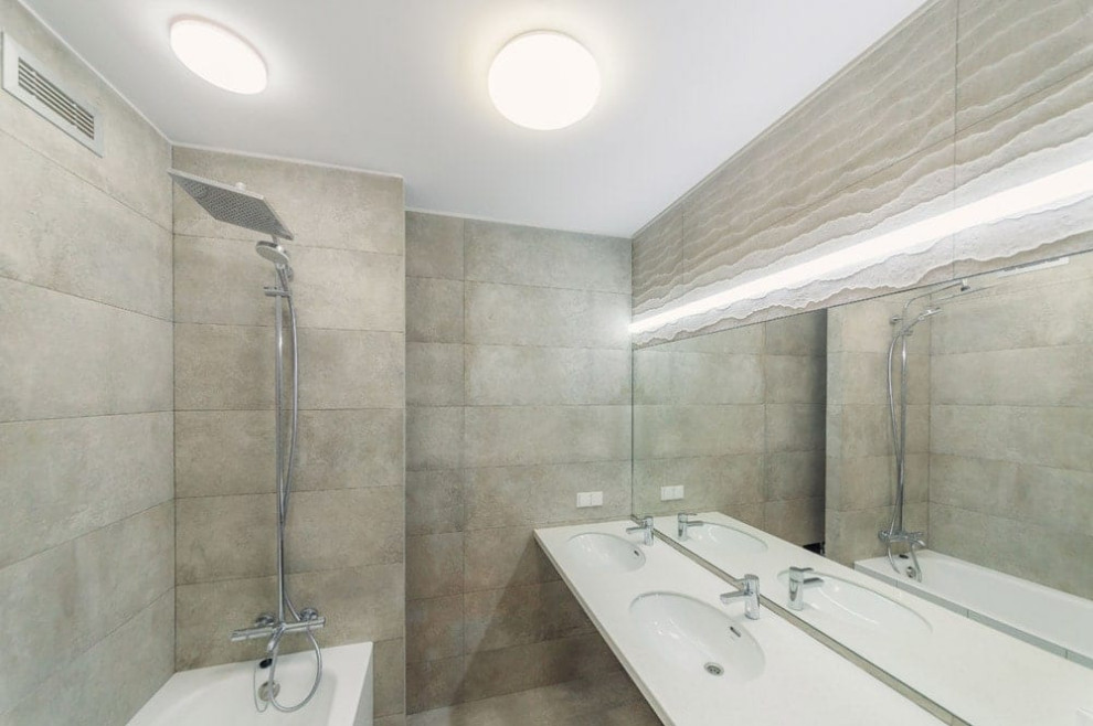 Свежая идея для дизайна: главная, серо-белая ванная комната среднего размера в современном стиле с белыми фасадами, полновстраиваемой ванной, душем над ванной, серой плиткой, керамической плиткой, серыми стенами, полом из керамогранита, раковиной с несколькими смесителями, столешницей из искусственного камня, серым полом, открытым душем, белой столешницей, зеркалом с подсветкой, тумбой под две раковины и подвесной тумбой - отличное фото интерьера
