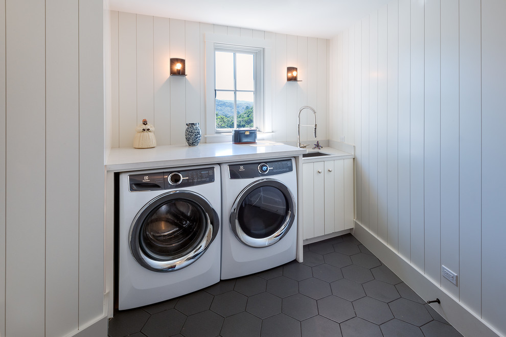 This is an example of a country utility room in San Francisco with an undermount sink, flat-panel cabinets, white cabinets, quartz benchtops, white walls, porcelain floors, a side-by-side washer and dryer and grey floor.