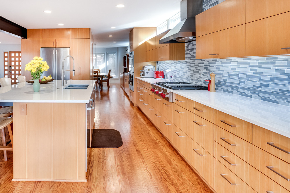 Mid-sized contemporary l-shaped open plan kitchen in Kansas City with flat-panel cabinets, light wood cabinets, quartz benchtops, glass tile splashback, stainless steel appliances, medium hardwood floors, with island, brown floor, white benchtop, a double-bowl sink and blue splashback.