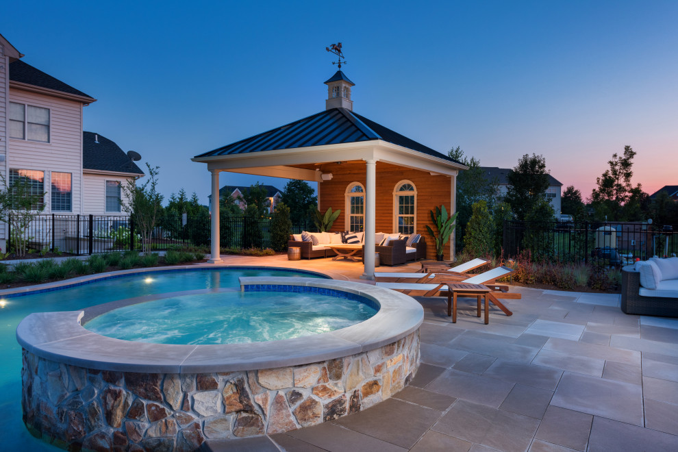 Modelo de piscinas y jacuzzis naturales tradicionales grandes redondeados en patio trasero con adoquines de piedra natural