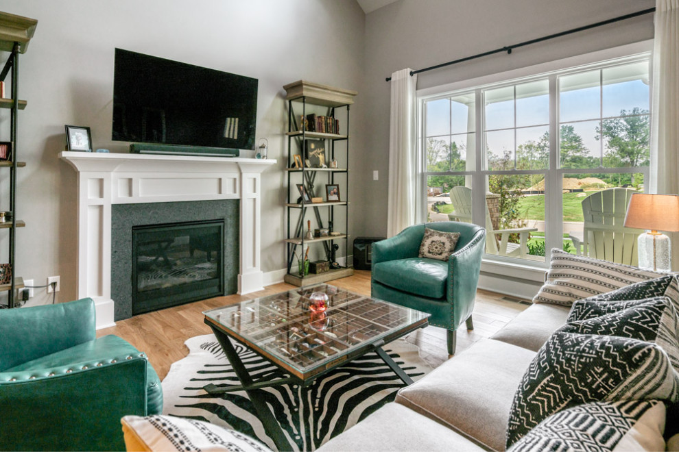 Inspiration for a country open concept living room in Louisville with a music area, grey walls, medium hardwood floors, a standard fireplace, a wood fireplace surround, a wall-mounted tv, brown floor and vaulted.