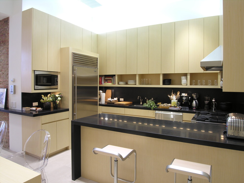 Photo of a modern u-shaped eat-in kitchen in New York with flat-panel cabinets, light wood cabinets, black splashback and stainless steel appliances.