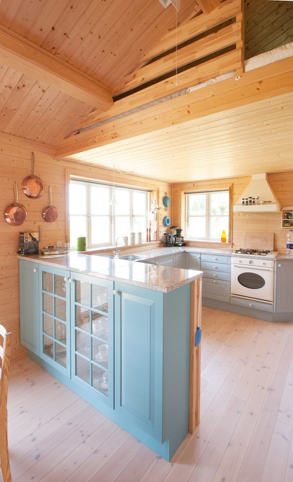 This is an example of a mid-sized country u-shaped kitchen in Esbjerg with blue cabinets, granite benchtops, beige splashback, timber splashback, light hardwood floors, beige floor, raised-panel cabinets, white appliances, a peninsula and grey benchtop.