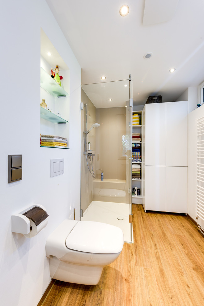 Mid-sized contemporary 3/4 bathroom in Hamburg with flat-panel cabinets, white cabinets, a curbless shower, a wall-mount toilet, white tile, ceramic tile, white walls, painted wood floors, a vessel sink, solid surface benchtops, brown floor, a sliding shower screen and white benchtops.