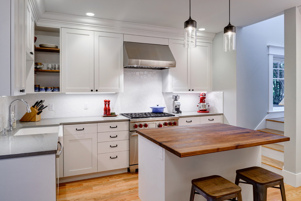 Design ideas for a transitional l-shaped kitchen in Seattle with a farmhouse sink, shaker cabinets, white cabinets, white splashback, stainless steel appliances, medium hardwood floors and with island.