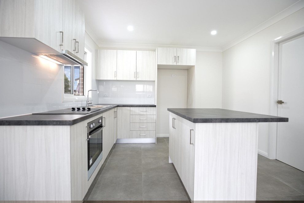 Small contemporary l-shaped open plan kitchen in Sydney with a double-bowl sink, grey cabinets, laminate benchtops, white splashback, porcelain splashback, stainless steel appliances, ceramic floors, grey floor, black benchtop and with island.