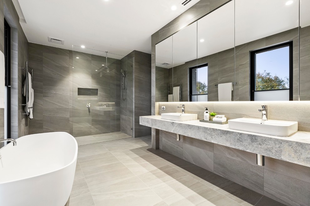 Design ideas for a mid-sized contemporary master bathroom in Melbourne with glass-front cabinets, grey cabinets, a freestanding tub, an open shower, a wall-mount toilet, gray tile, porcelain tile, grey walls, porcelain floors, a console sink, limestone benchtops, grey floor, an open shower and grey benchtops.