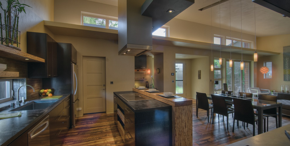 Small transitional galley medium tone wood floor and brown floor open concept kitchen photo with an undermount sink, flat-panel cabinets, dark wood cabinets, concrete countertops, gray backsplash, ceramic backsplash, stainless steel appliances, an island and gray countertops