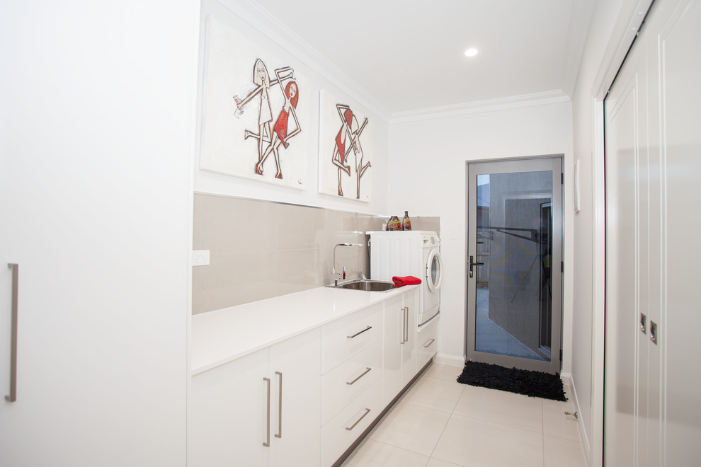 Design ideas for a mid-sized contemporary single-wall dedicated laundry room in Other with a single-bowl sink, white cabinets, white walls, flat-panel cabinets, granite benchtops, beige splashback, ceramic splashback, ceramic floors, white floor and white benchtop.