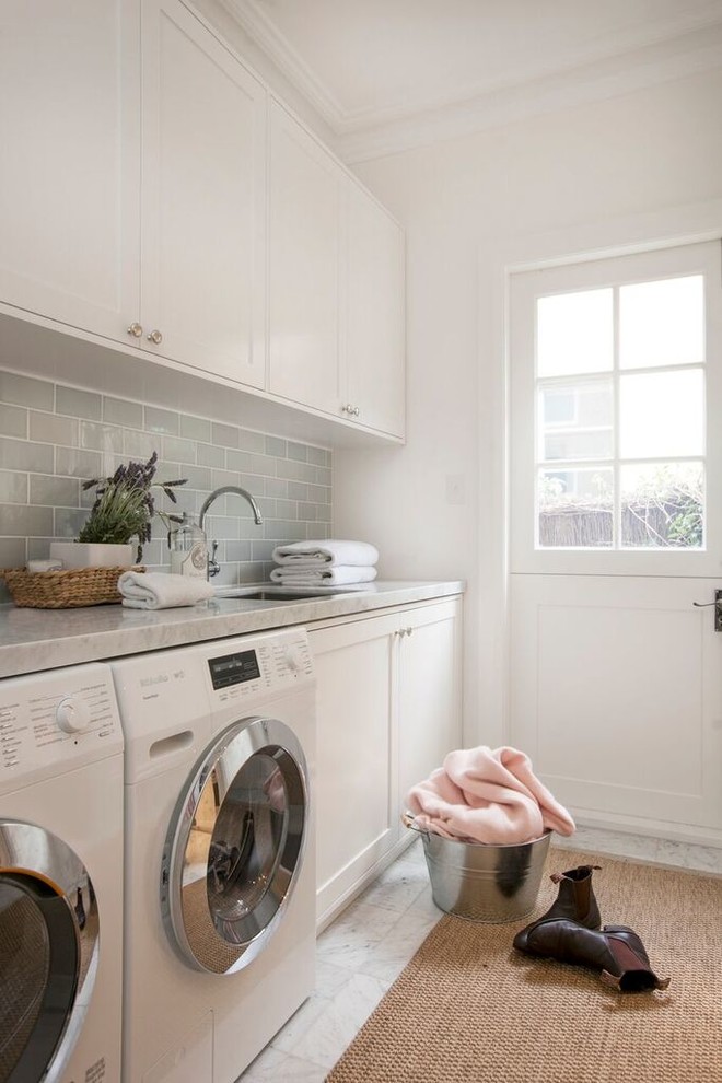 This is an example of a mid-sized transitional dedicated laundry room in Sydney with an undermount sink, white cabinets, marble benchtops, grey walls, medium hardwood floors, a side-by-side washer and dryer and recessed-panel cabinets.
