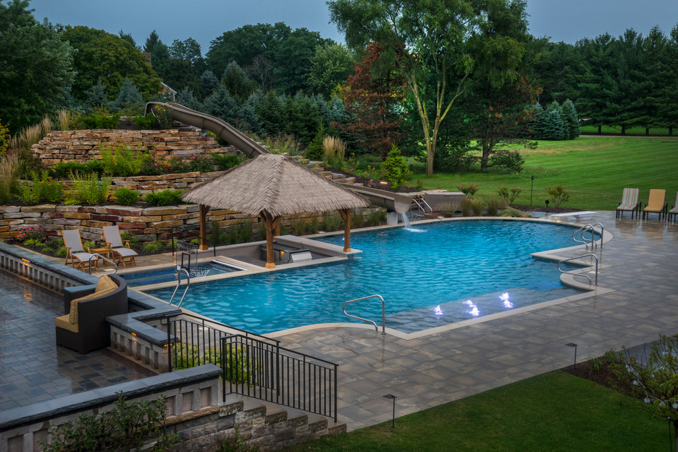 Design ideas for an expansive tropical backyard custom-shaped lap pool in Chicago with a water slide and natural stone pavers.