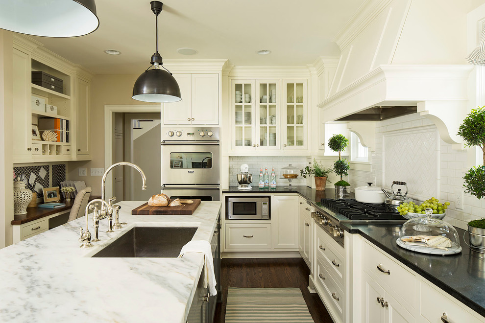Elegant dark wood floor kitchen photo in Minneapolis with an undermount sink, glass-front cabinets, white cabinets, white backsplash, subway tile backsplash, stainless steel appliances and an island